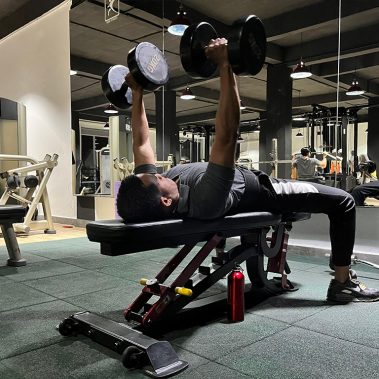 Seorang member pria di BisaFitness sedang melakukan latihan dumbbell press di atas bench, fokus memperkuat otot dada dan lengan di area gym yang bersih dan tertata rapi. BisaFitness adalah gym dan fitness center di Batam yang ramah untuk pemula, bersih, dan affordable, dengan dua cabang terdekat di Tiban dan Batam Center.