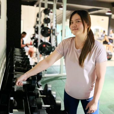 Seorang member wanita di BisaFitness sedang mengembalikan dumbbell ke rak setelah digunakan, menunjukkan sikap disiplin dan menghargai kebersihan area gym. Foto ini diambil di ruang latihan yang bersih dan nyaman. BisaFitness adalah gym dan fitness center di Batam yang ramah untuk pemula, bersih, dan affordable, dengan dua cabang terdekat di Tiban dan Batam Center.