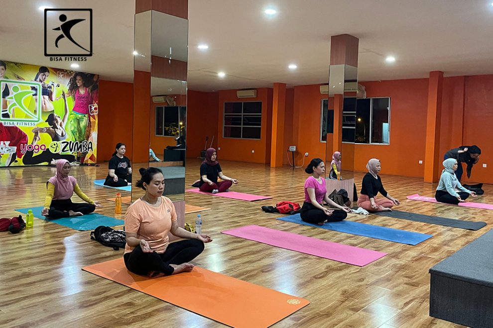 Peserta kelas yoga di BisaFitness, gym di Pulau Batam, sedang berpose duduk bersila dalam posisi meditasi. Dengan mata tertutup dan tubuh yang tenang, mereka menciptakan suasana damai dan fokus, menunjukkan manfaat mental dan fisik dari latihan yoga. BisaFitness menawarkan kelas yoga untuk meningkatkan kesehatan dan kebugaran anggota