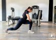Member BisaFitness sedang melakukan stretching di gym dengan posisi lunges untuk meningkatkan fleksibilitas tubuh, di ruangan bersih dan nyaman dilengkapi peralatan olahraga modern.