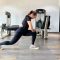 Member BisaFitness sedang melakukan stretching di gym dengan posisi lunges untuk meningkatkan fleksibilitas tubuh, di ruangan bersih dan nyaman dilengkapi peralatan olahraga modern.