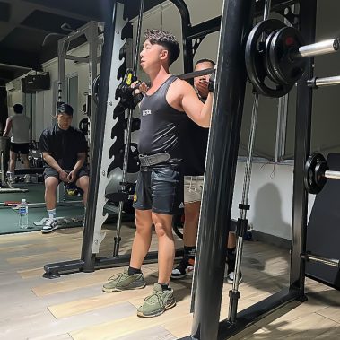 Seorang member BISA Fitness sedang berlatih squat menggunakan smith machine dengan pendampingan personal trainer di gym yang luas dan bersih. BISA Fitness adalah gym dan fitness center yang ramah pemula, bersih, dan affordable dengan dua cabang terdekat di Tiban dan Batam Center.