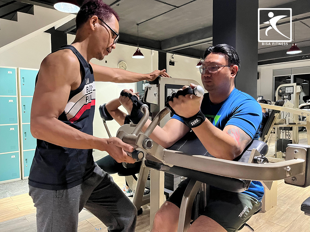 Trainer in Bisa Fitness with a member using biceps curl machine